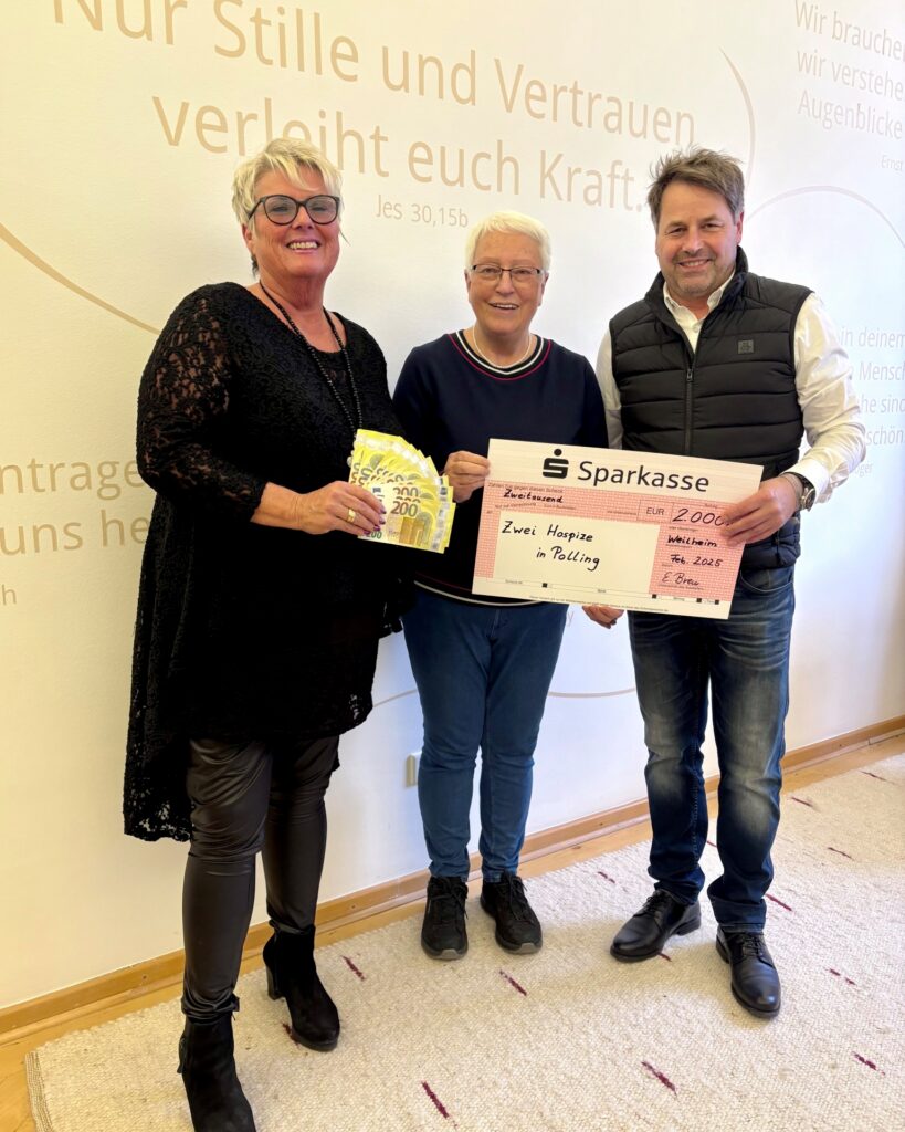 Heller Aufenthaltsraum, Spendenübergabe an Hospiz Polling. Drei Personen lächeln.