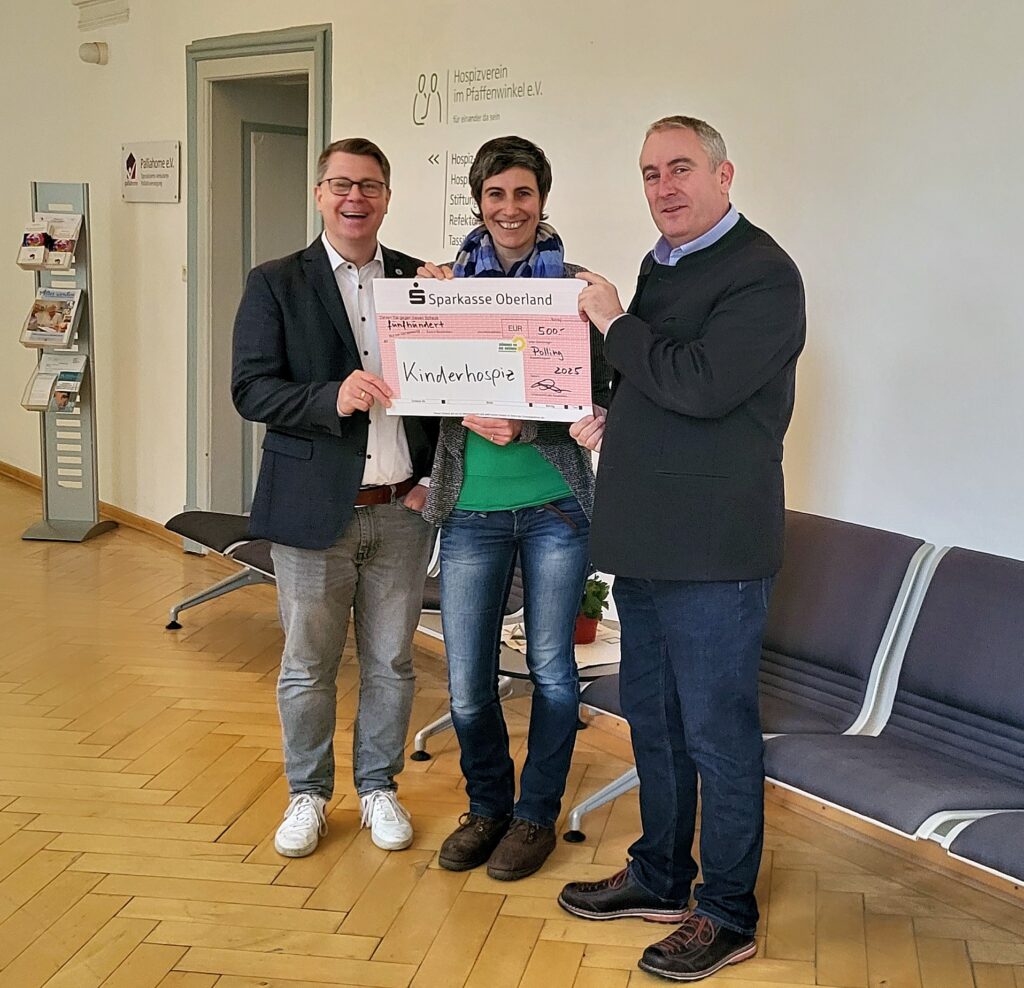 Drei lächelnde Personen mit Spendencheck im hellen Raum, Hospiz Polling.