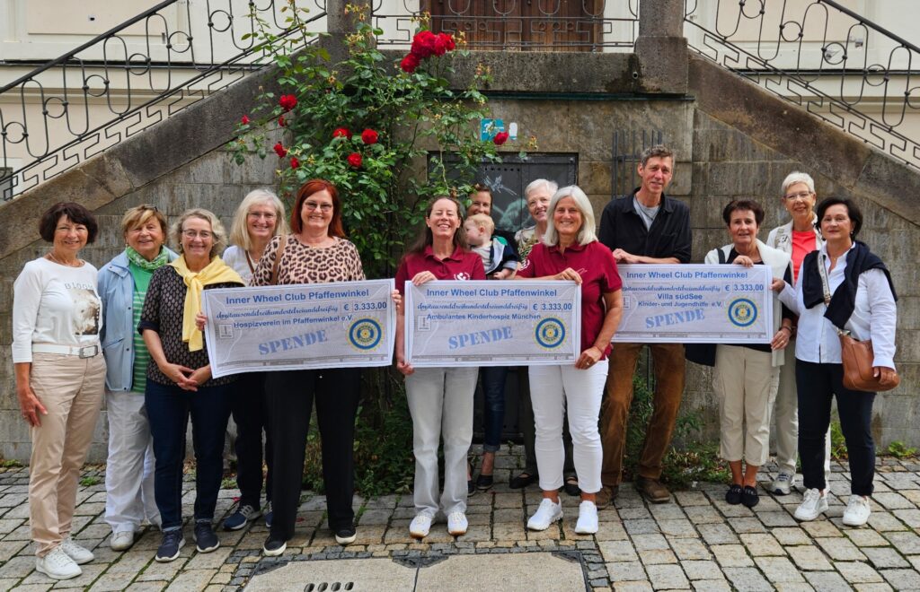 Hospiz Polling - Hospizverein Pfaffenwinkel: Spendenübergabe, Gruppe vor Steinwand und Rosenbusch.
