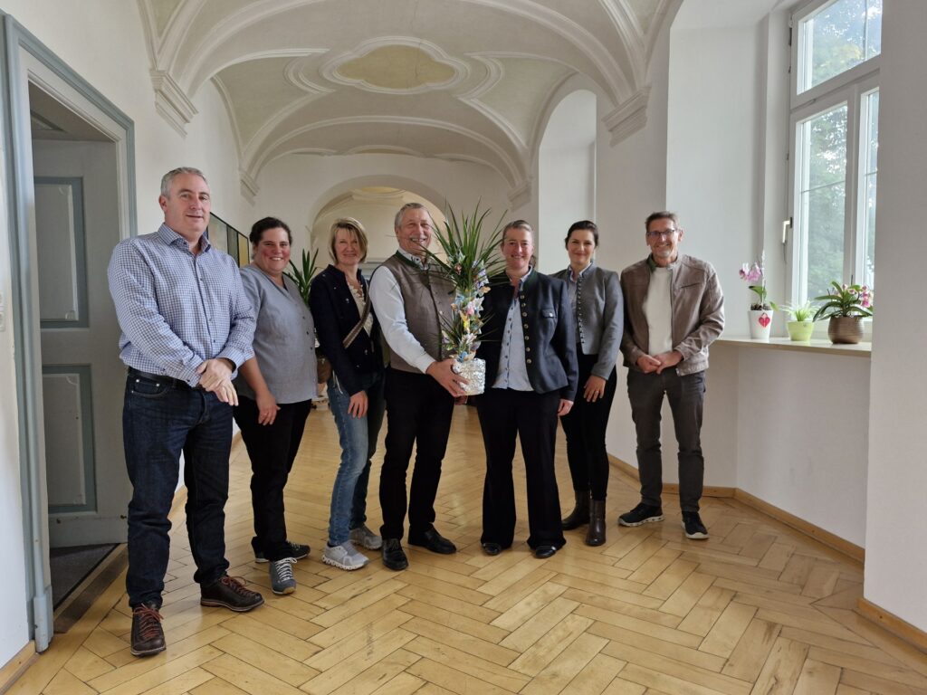 Heller Flur bei Hospiz Polling, lächelnde Gruppe mit Blumenarrangement.