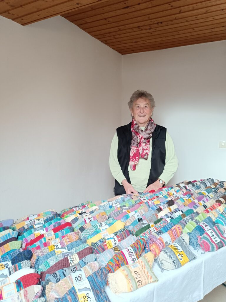 Heller Gemeinschaftsraum, Frau verkauft bunte Stricksocken für Hospiz Polling.