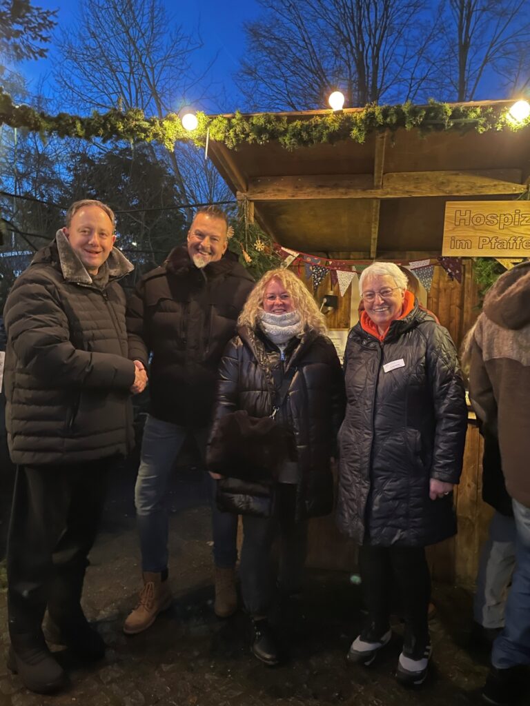 Vier Erwachsene vor weihnachtlichem Hospiz Polling - Hospizverein Pfaffenwinkel-Stand.
