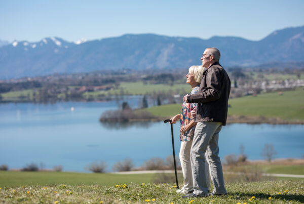 Älteres Paar auf Hügel, blickt zum See; Berge bei Hospiz Polling.