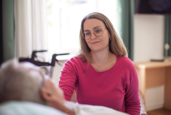 Pflegekraft tröstet Patientin im hellen Zimmer, Hospiz Polling.