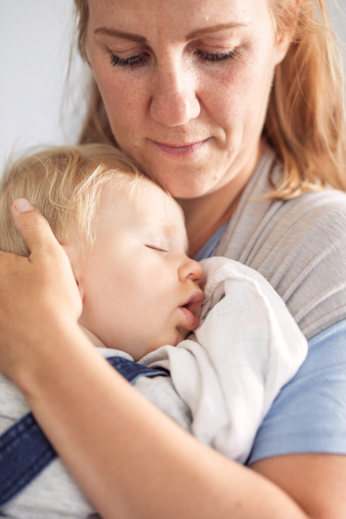 Mitarbeiterin hält schlafendes Baby im Arm, beide entspannt. Mitarbeiterin hält schlafendes Baby im Arm, beide entspannt.