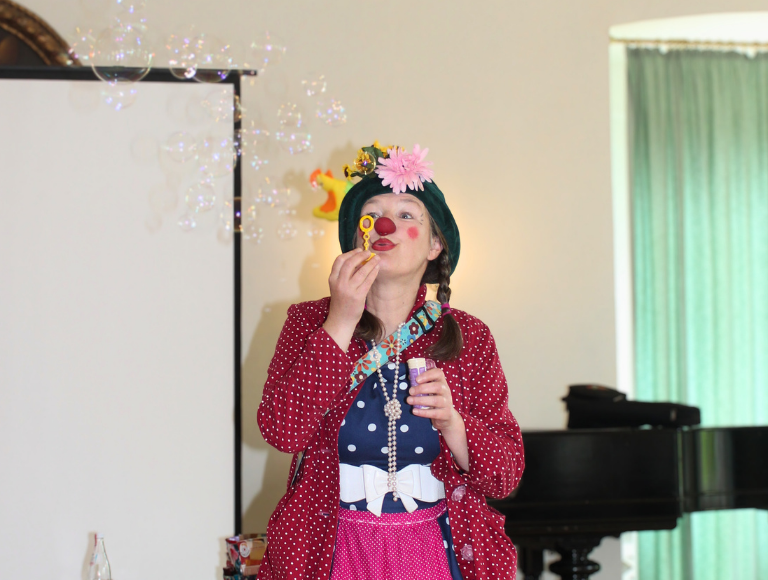 Bunter Clown macht Seifenblasen im Veranstaltungsraum, entspannte Atmosphäre.