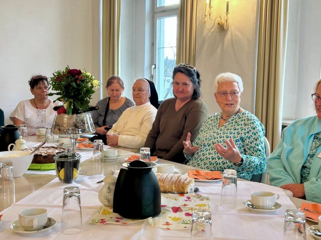 Frauenrunde beim Kaffeetrinken, Sonnenlicht durchflutet Aufenthaltsraum, lebendige Unterhaltung.
