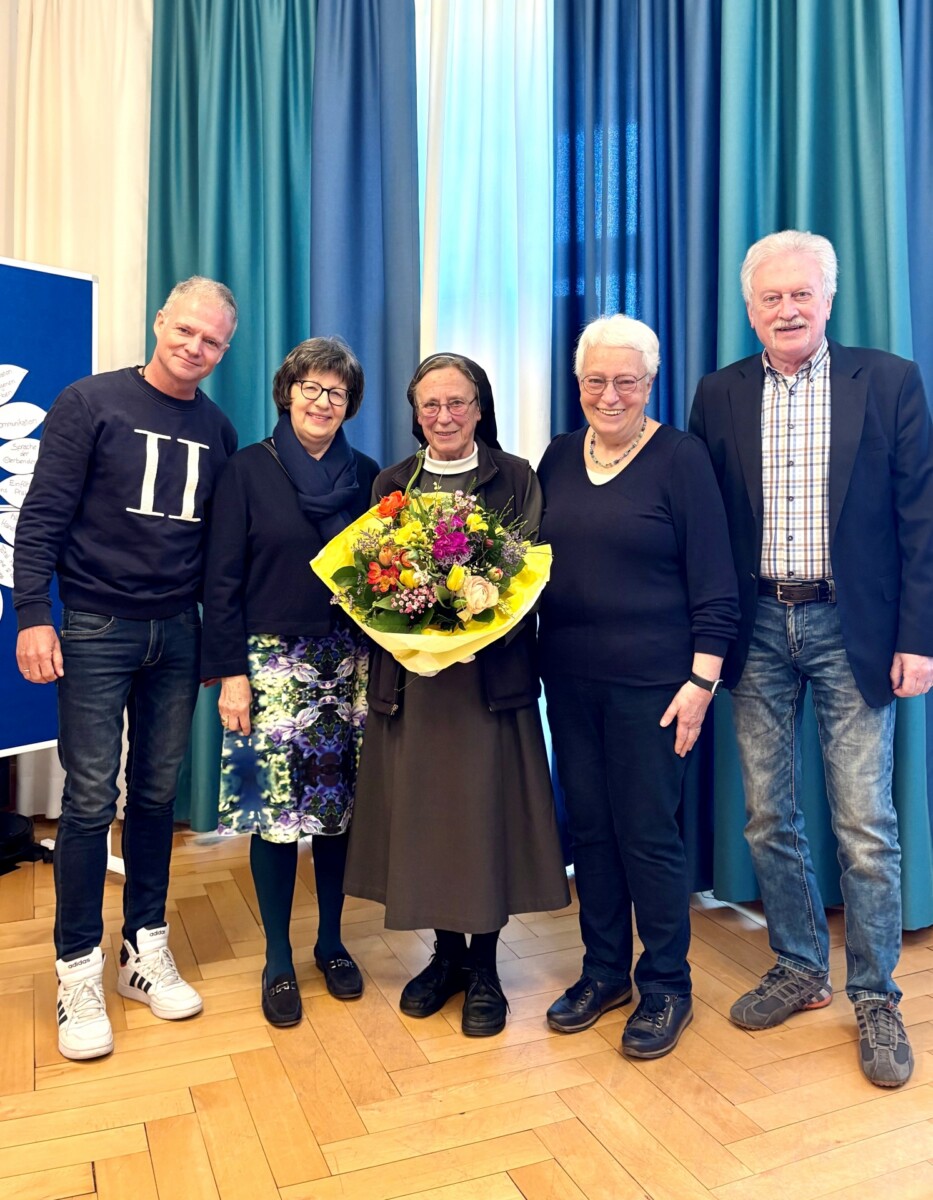 Sr. Angela Kirchensteiner mit Blumenstrauß, Gruppe lächelt, festliche Atmosphäre.